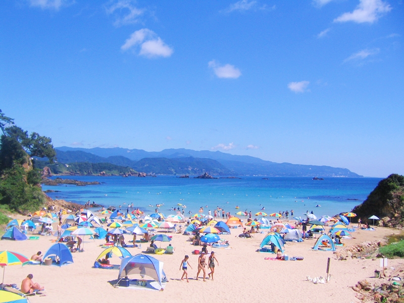 青い空と海、砂浜に海水浴客が多くいる